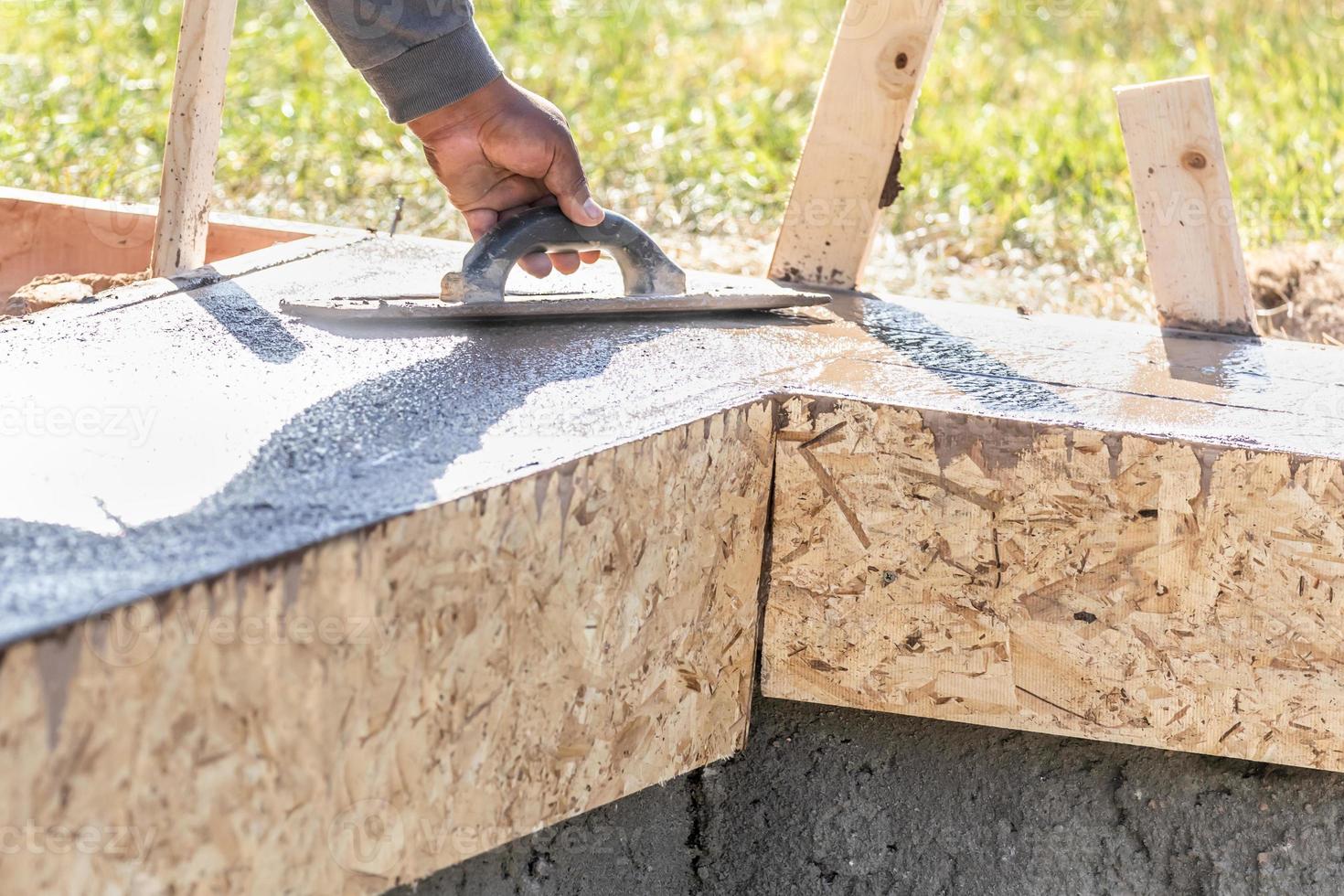 Construction Worker Using Wood Trowel On Wet Cement Forming Coping Around New Pool photo