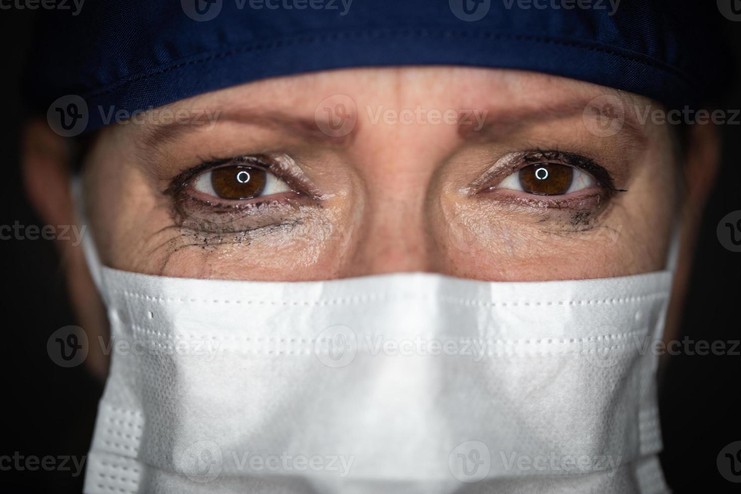 doctora o enfermera estresada y llorosa con mascarilla médica en un fondo oscuro foto