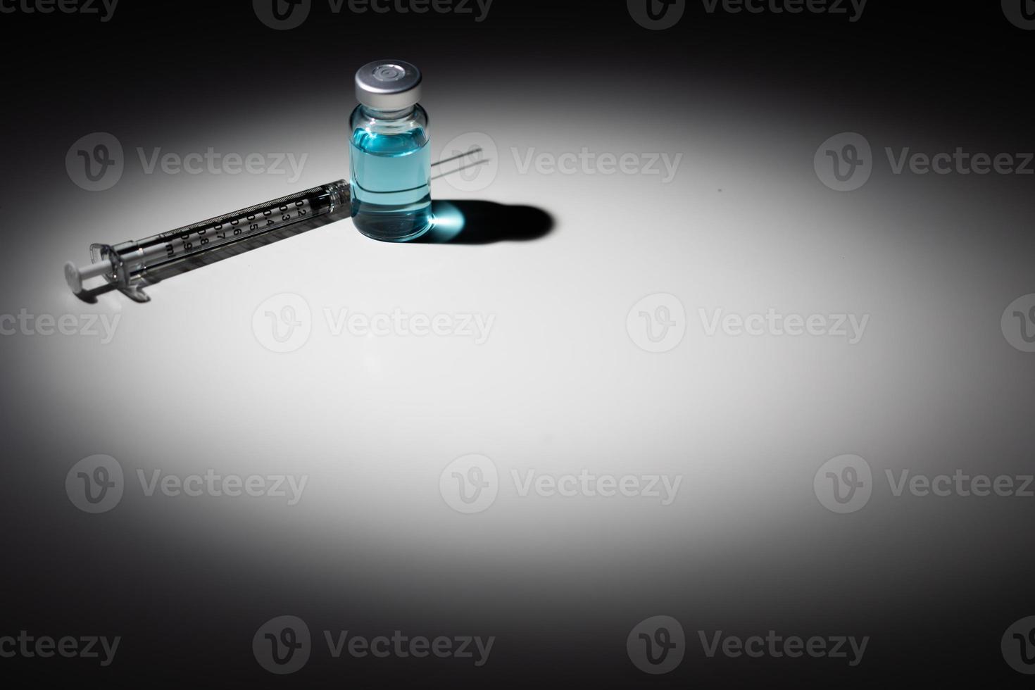 Syringe Needle and Medicine Vial With Light Blue Chemical Spot Lit on Reflective Background photo