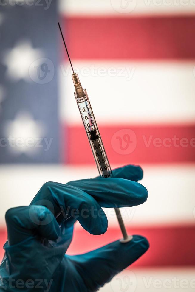 Front Line Worker Holding Syringe Filled with Coronavirus Vaccine or Medicine Silhouetted Against American Flag photo