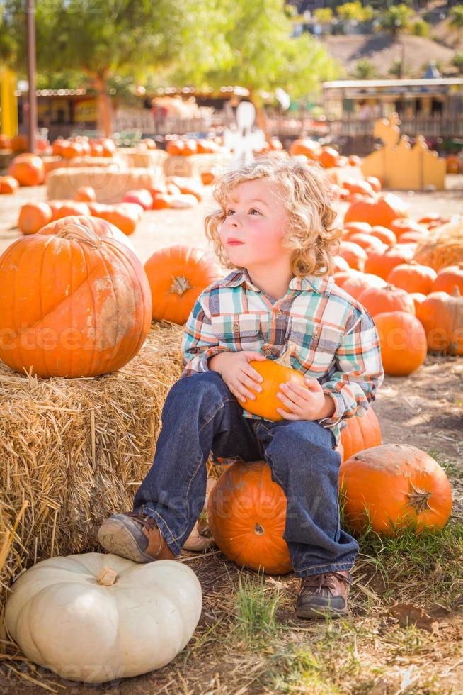 niño pequeño sentado y sosteniendo su calabaza en un rancho rústico en el huerto de calabazas. foto