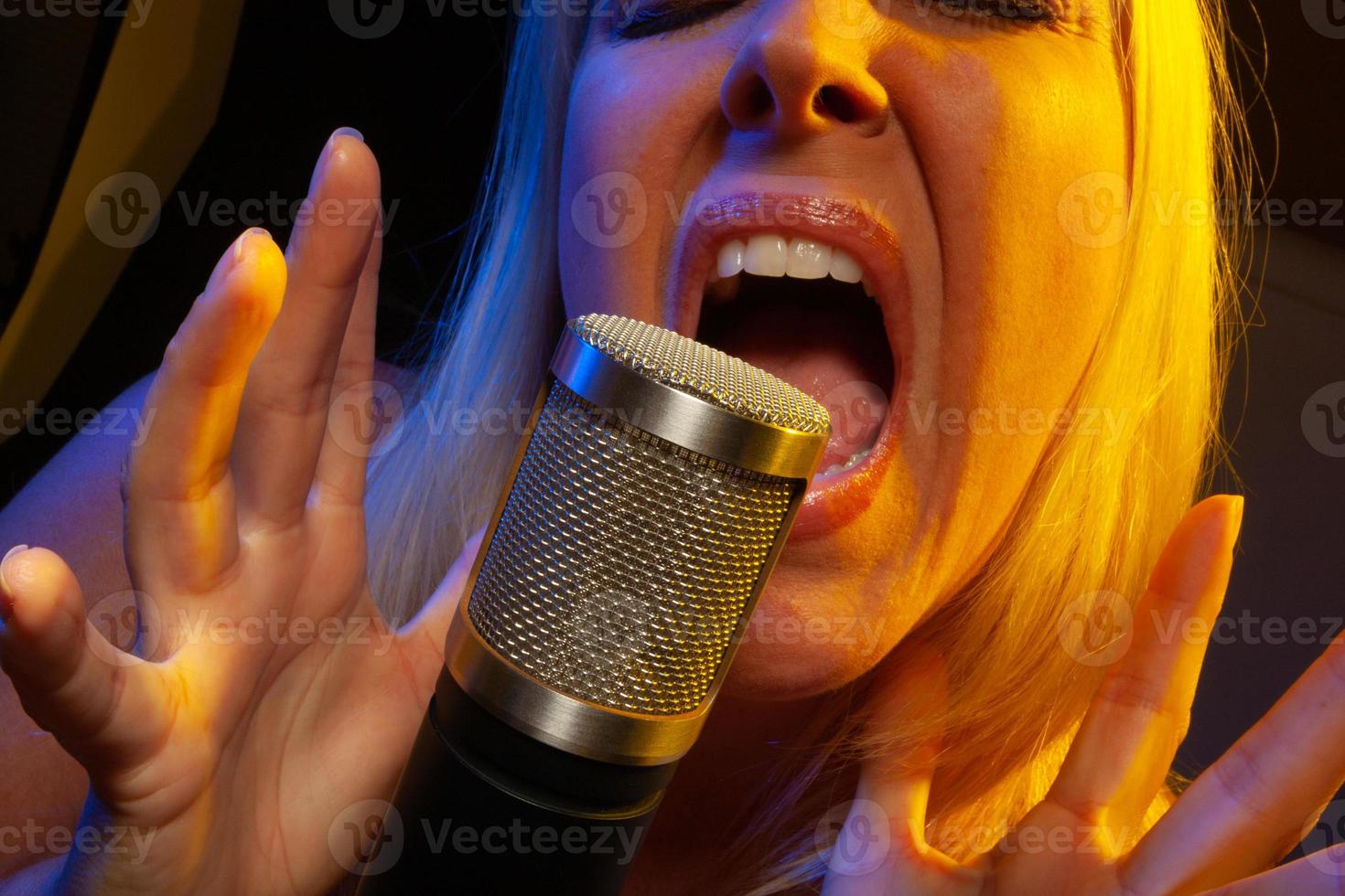 Female vocalist under gelled lighting sings with passion into condenser microphone. photo