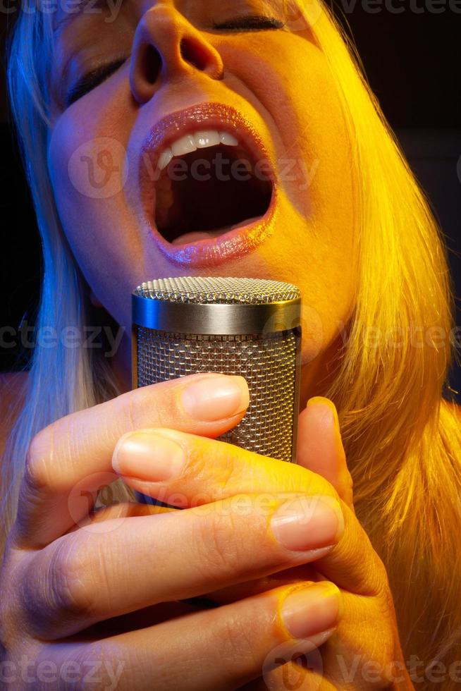 Female vocalist under gelled lighting sings with passion into condenser microphone. photo