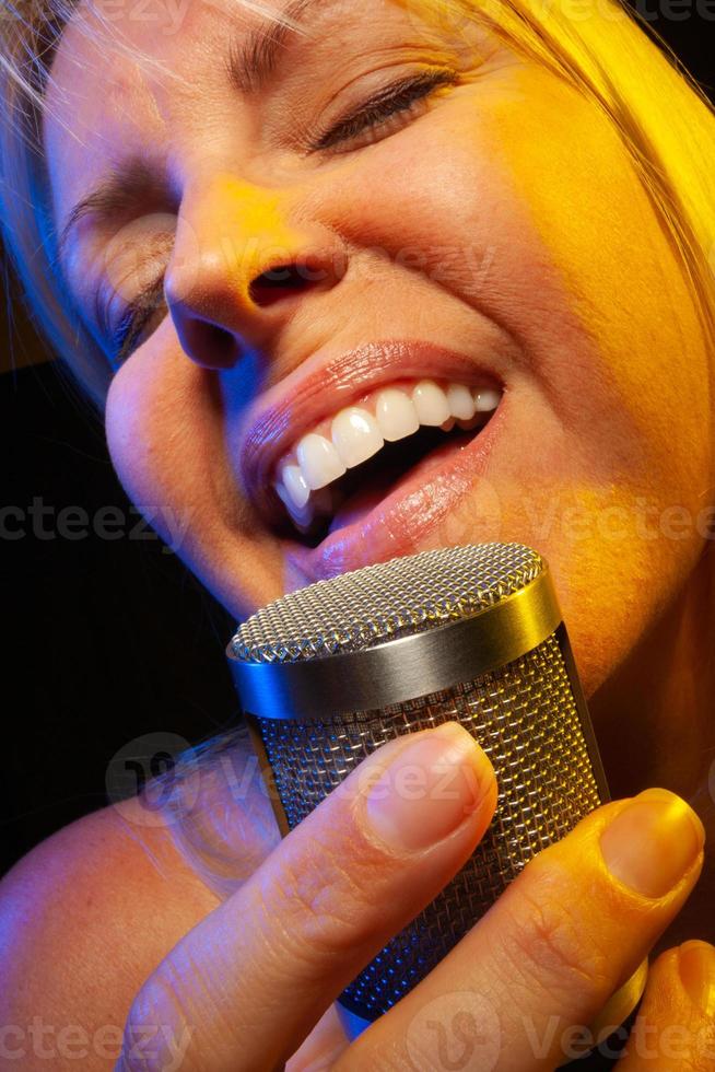 Female vocalist under gelled lighting sings with passion into condenser microphone. photo