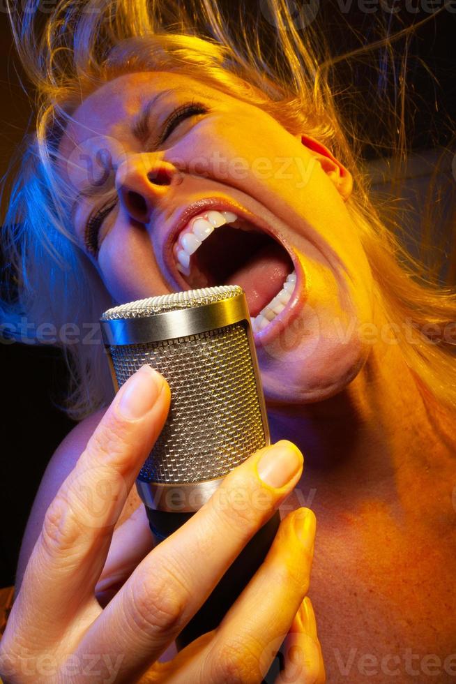 Female vocalist under gelled lighting sings with passion into condenser microphone. photo