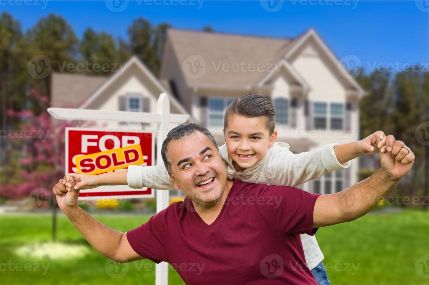 Hispanic Father and Mixed Race Son Having Fun In Front of House and Sold Real Estate Sign photo
