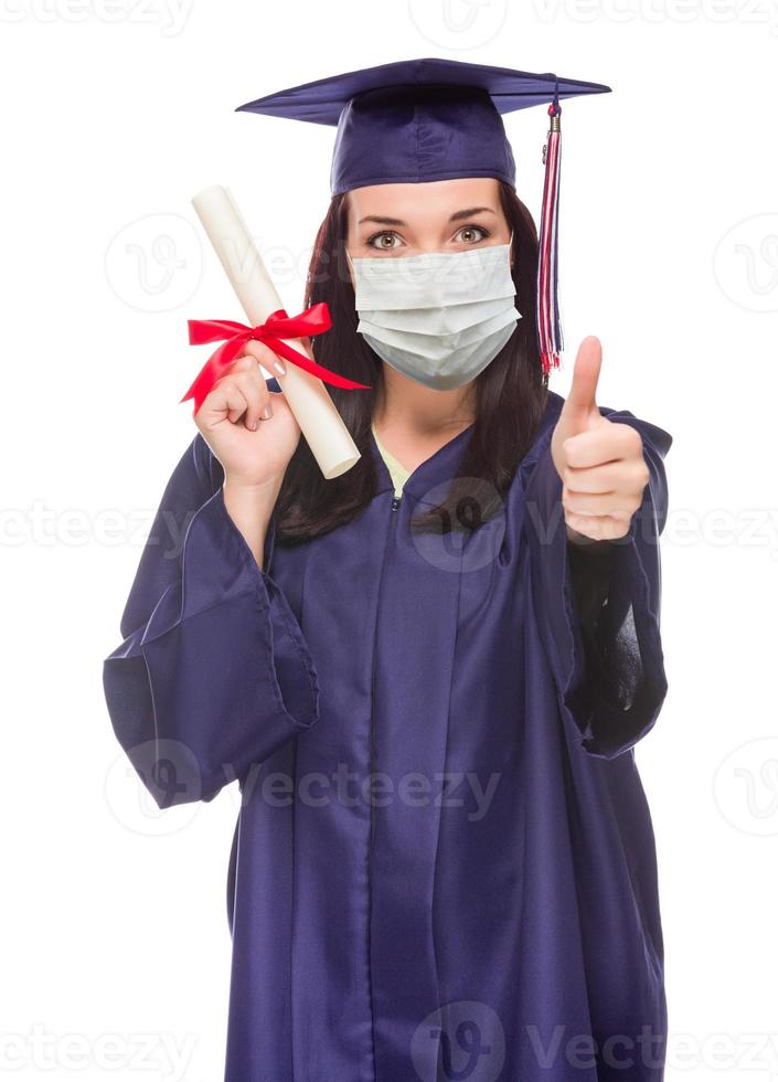 la mujer que se gradúa con mascarilla médica y toga y birrete da un pulgar hacia arriba aislada en un fondo blanco foto