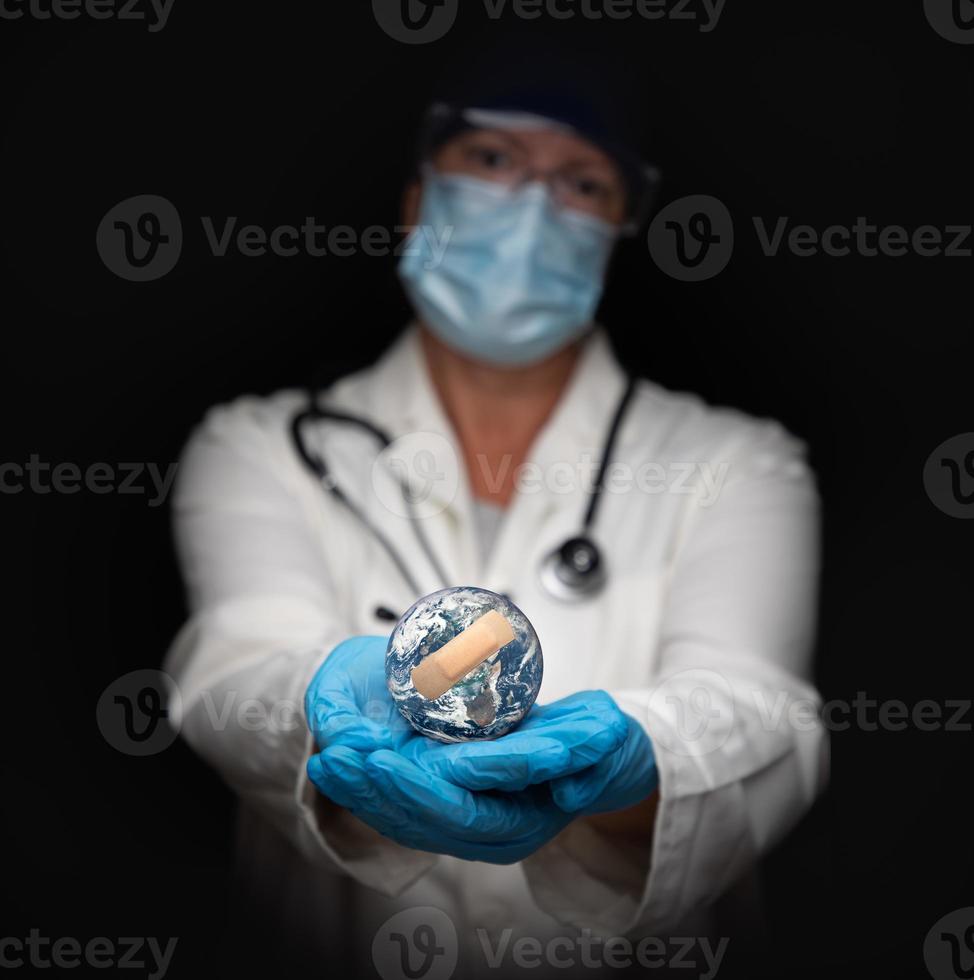 Nurse or Doctor Wearing Face Mask and Surgical Gloves Holding Bandaged Planet Earth photo