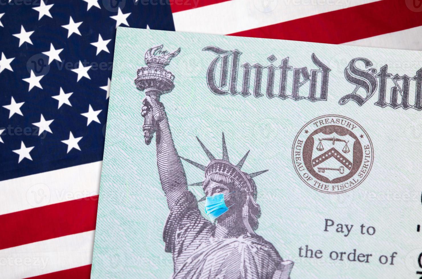 United States IRS Stimulus Check with Statue of Liberty Wearing Medical Face Mask Resting on American Flag photo