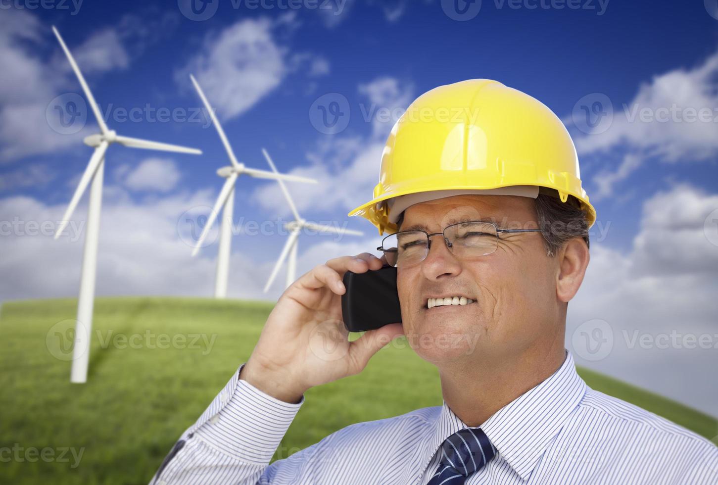Hard Hat Wearing Engineer on Phone with Turbines Behind photo
