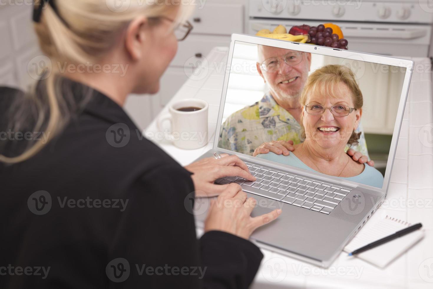 Woman In Kitchen Using Laptop - Online with Senior Couple photo