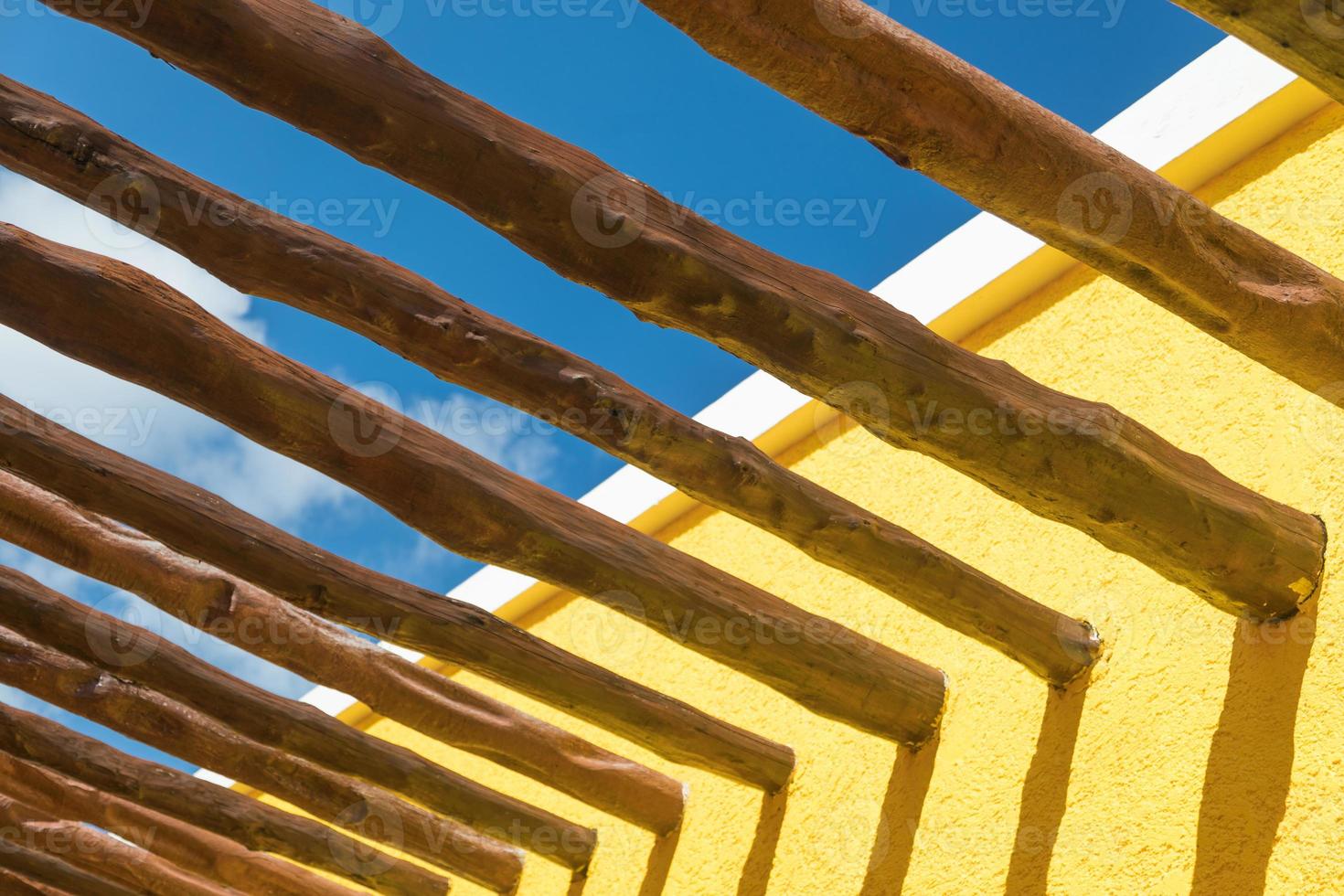 Abstract Wood Post Beams and Bright Yellow Wall Against Blue Sky photo
