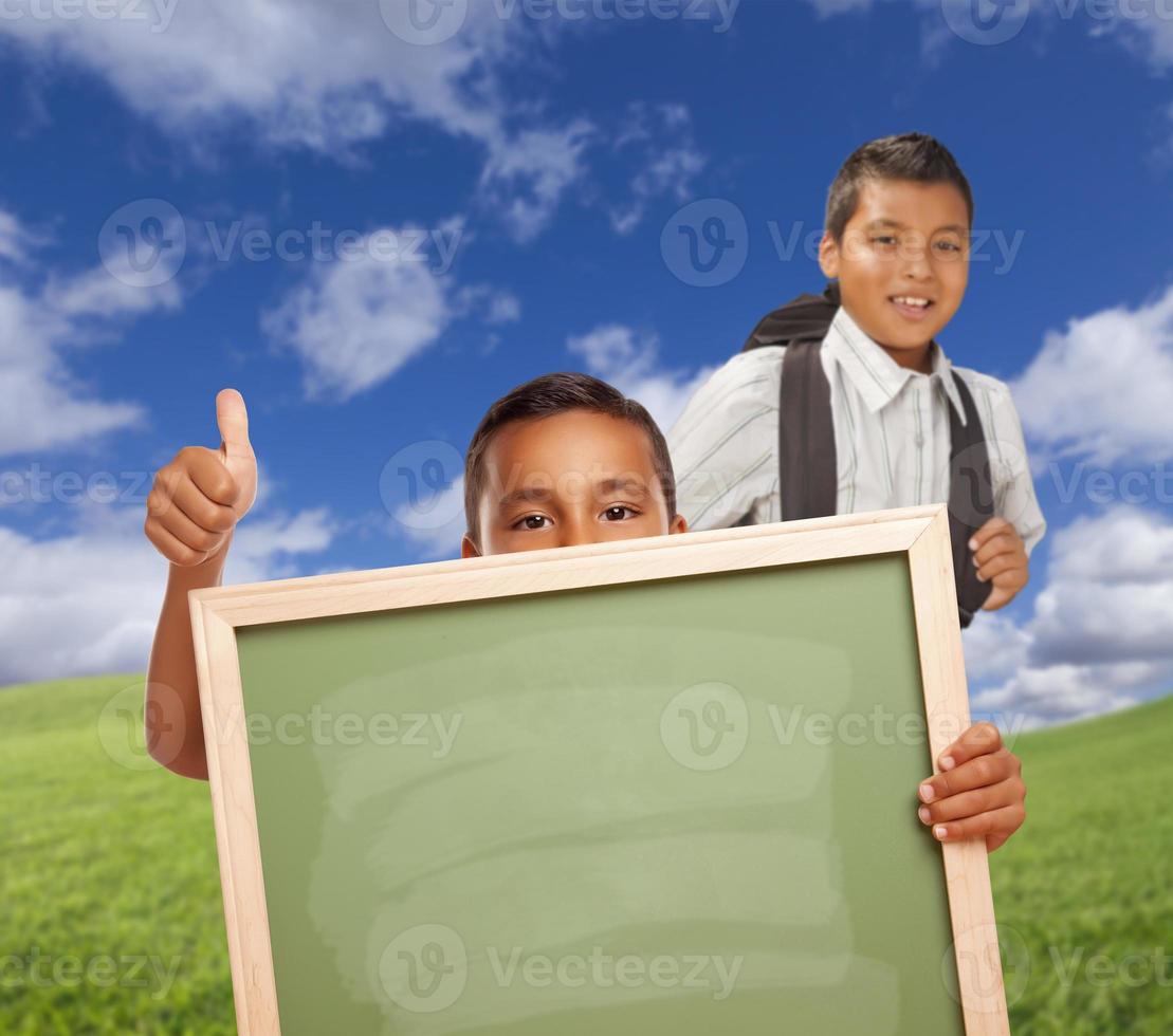 Students with Thumbs Up in Field Holding Blank Chalk Board photo