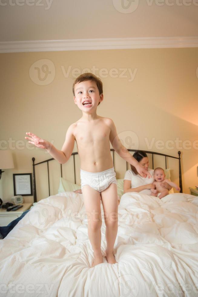 niño chino y caucásico de raza mixta saltando en la cama con su familia foto