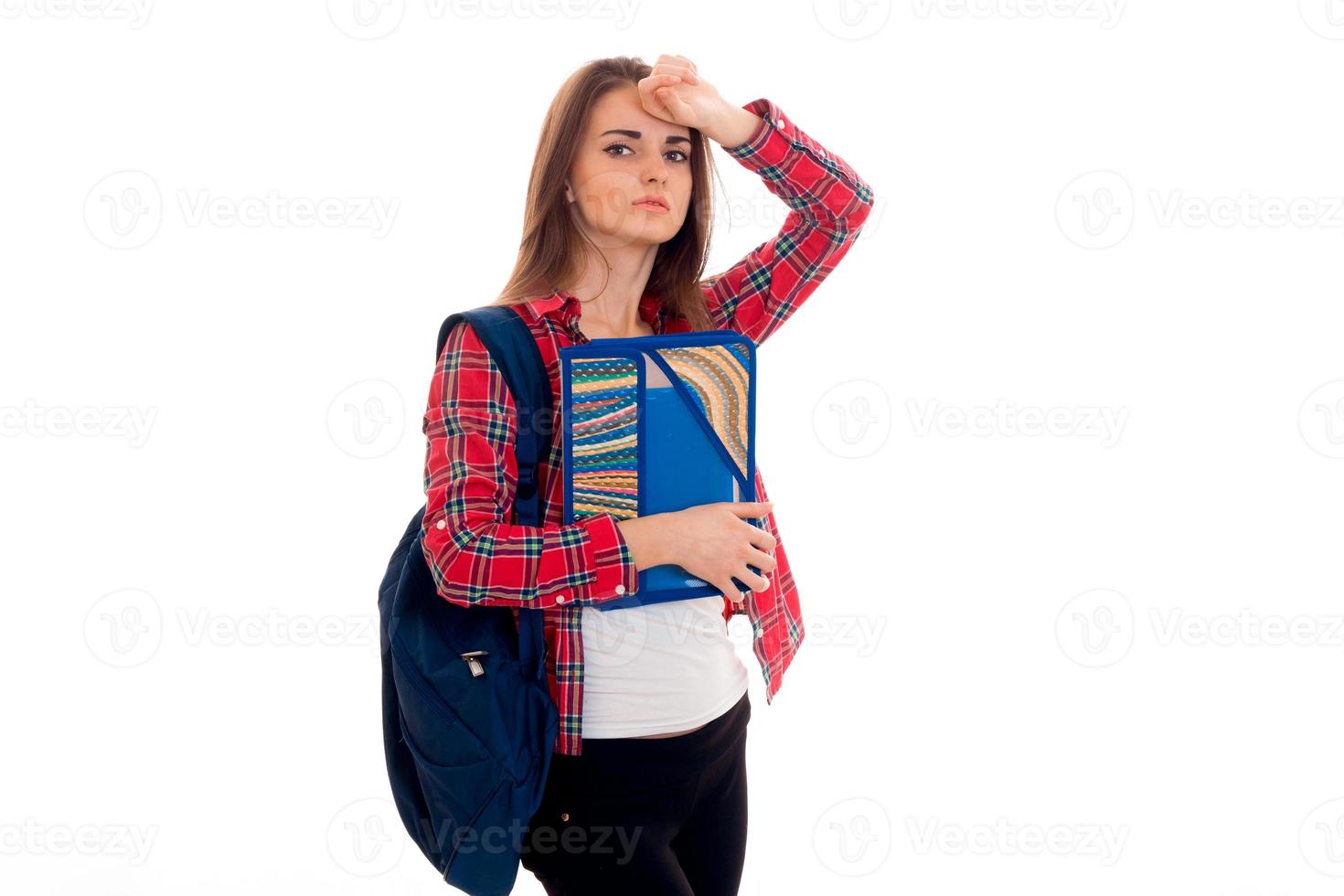 tired young students girl with backpack and folders for notebooks in her hands looking at the camera isolated on white background photo