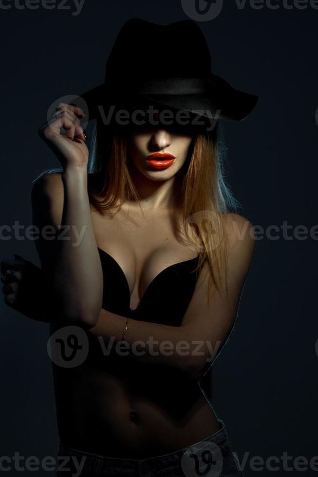 young girl in black bra with red lips wearing a hat with wide brim in studio photo