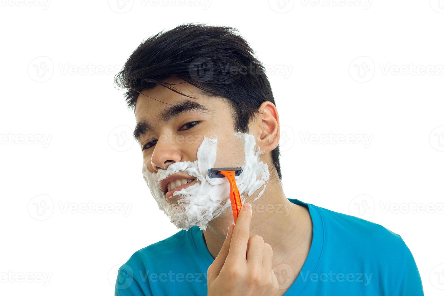 Un joven de pelo negro con espuma en la cara se afeita el primer plano de la máquina foto