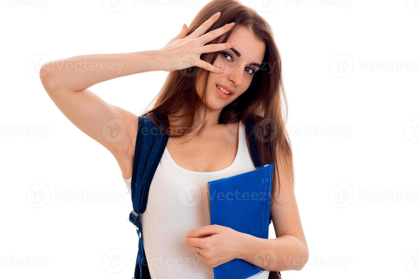 portrait of young displeased brunette student girl with backpack on her shoulders and books in her hands isolated on white background photo