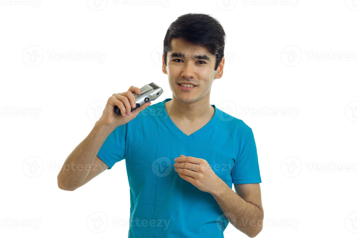 un chico guapo sonriente con la camisa azul se pone de pie y sostiene en su mano una maquinilla de afeitar foto