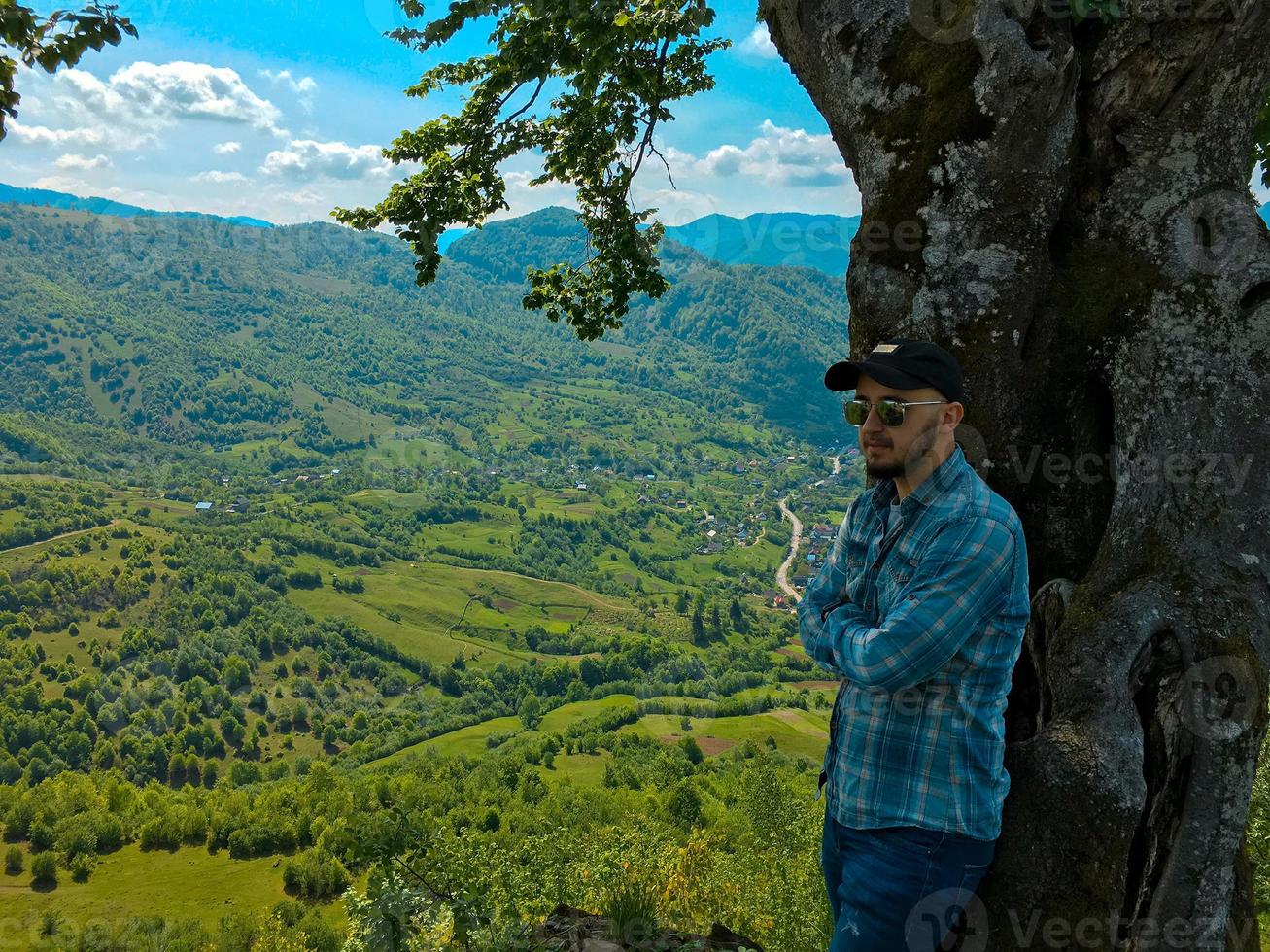 hombre posando cerca de un árbol con vistas a las montañas foto