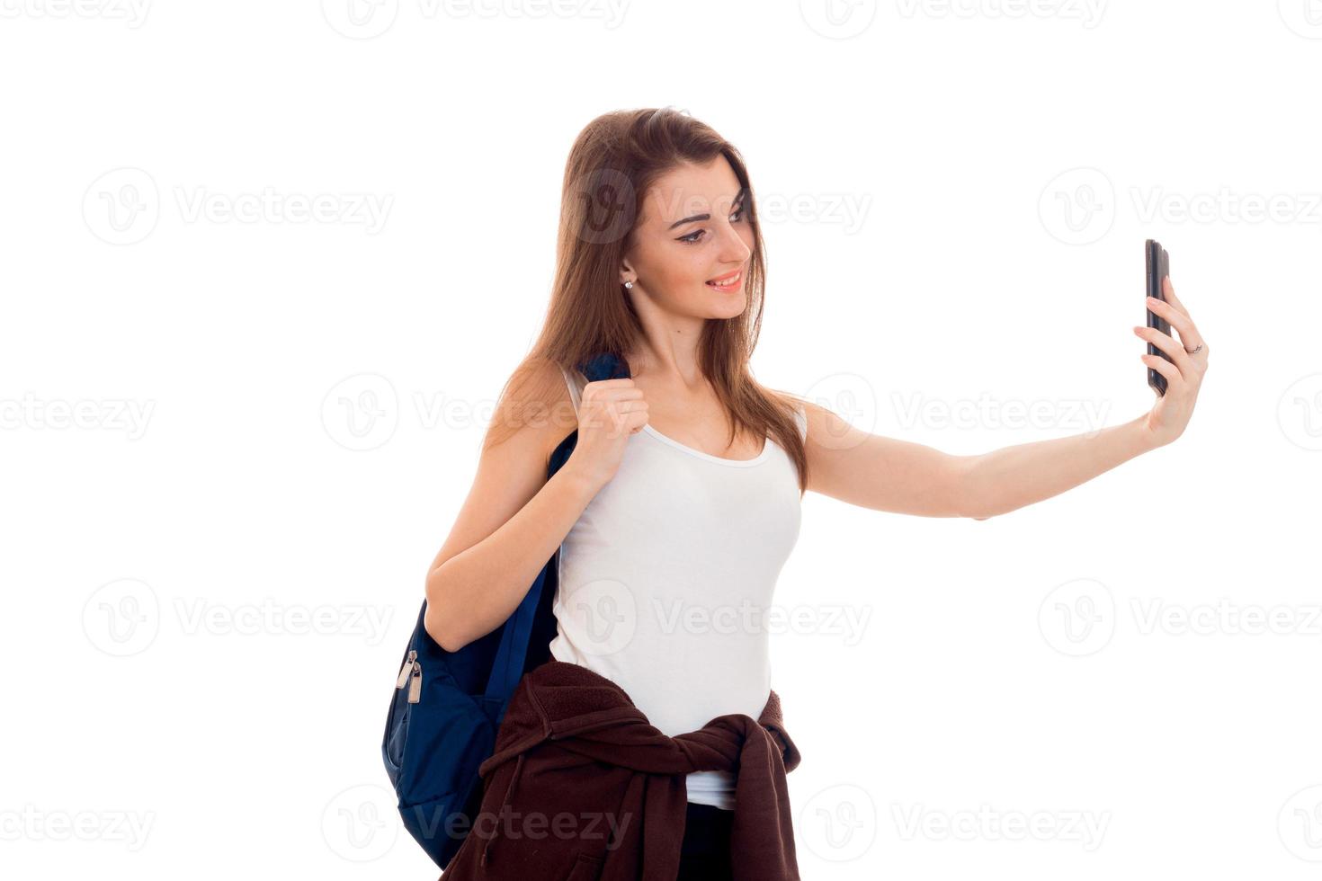 young smiling girl holding on his shoulder backpack and shoots himself on the phone photo