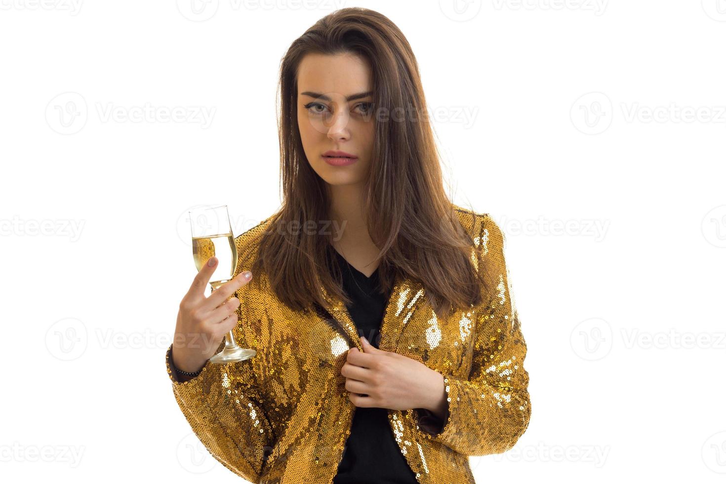 Serious girl in golden jacket with glass of wine in hands looks at the camera photo