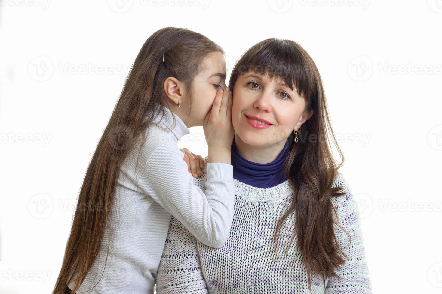 close-up portrait of a little girl who whispers something in his ear to her mum photo