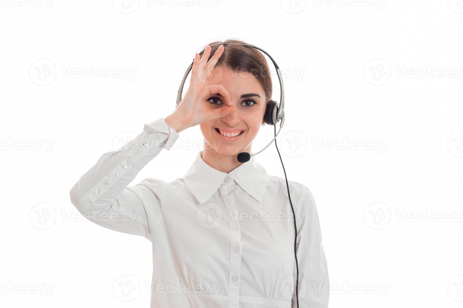 young girl in white shirt and headphones with microphone smiling keeps your hand near your eyes and looking at camera photo