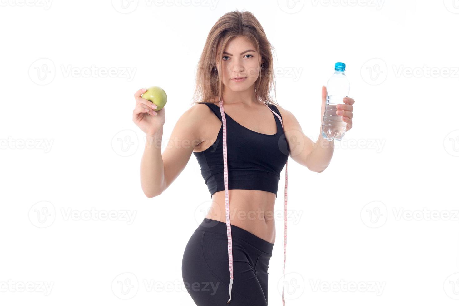 slim girl in a black top stretched out both hands forward shows a fruit and a bottle of water photo