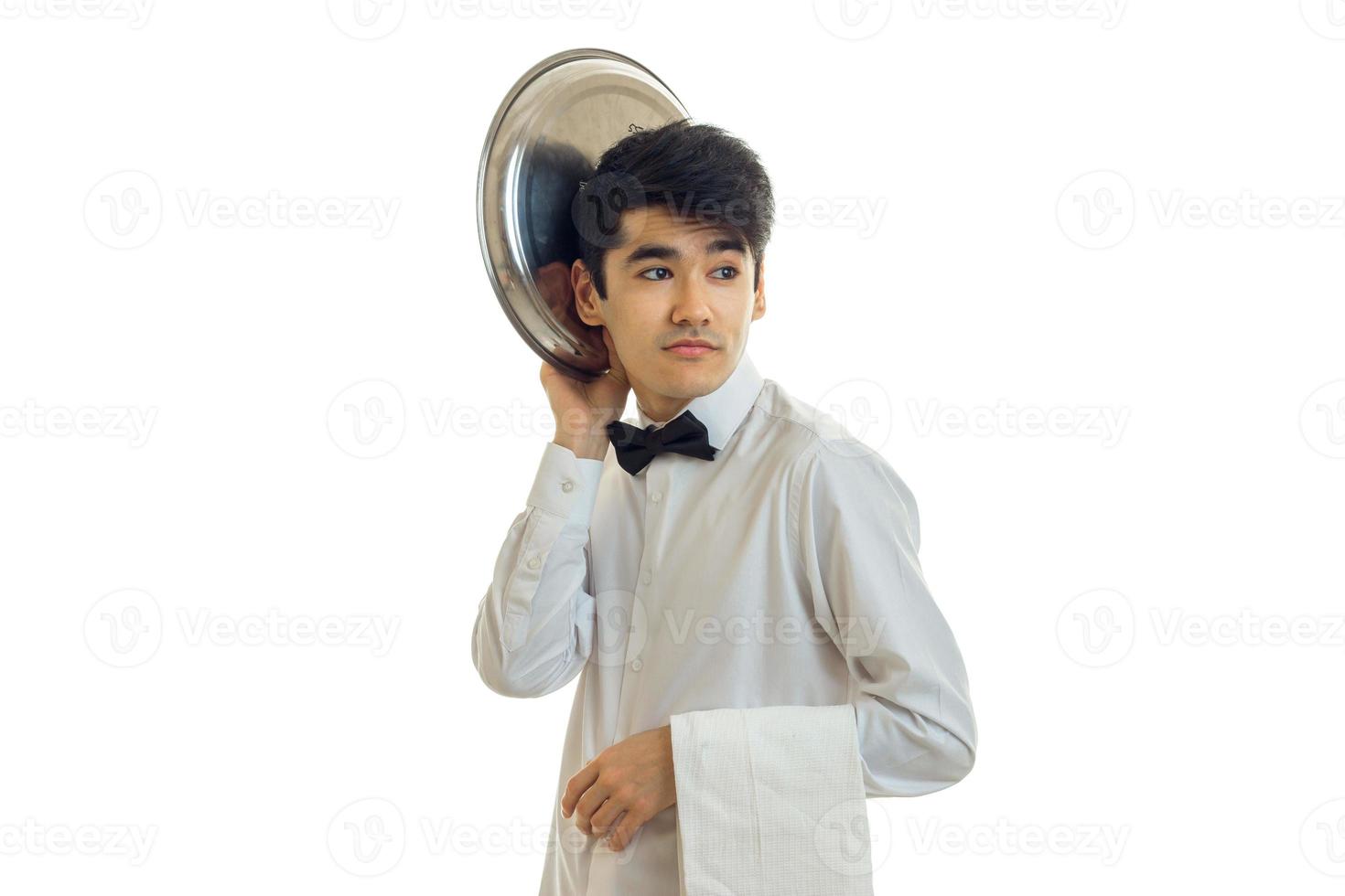 funny handsome waiter looks away and keeps the dish tray near his head isolated on white background photo