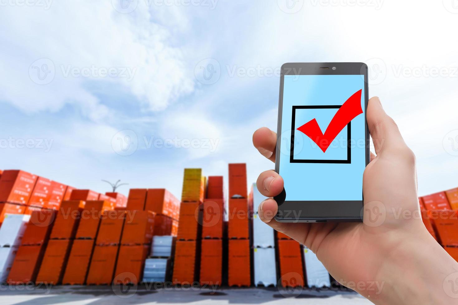 Hand holding smartphone against shelves with boxes in warehouse photo