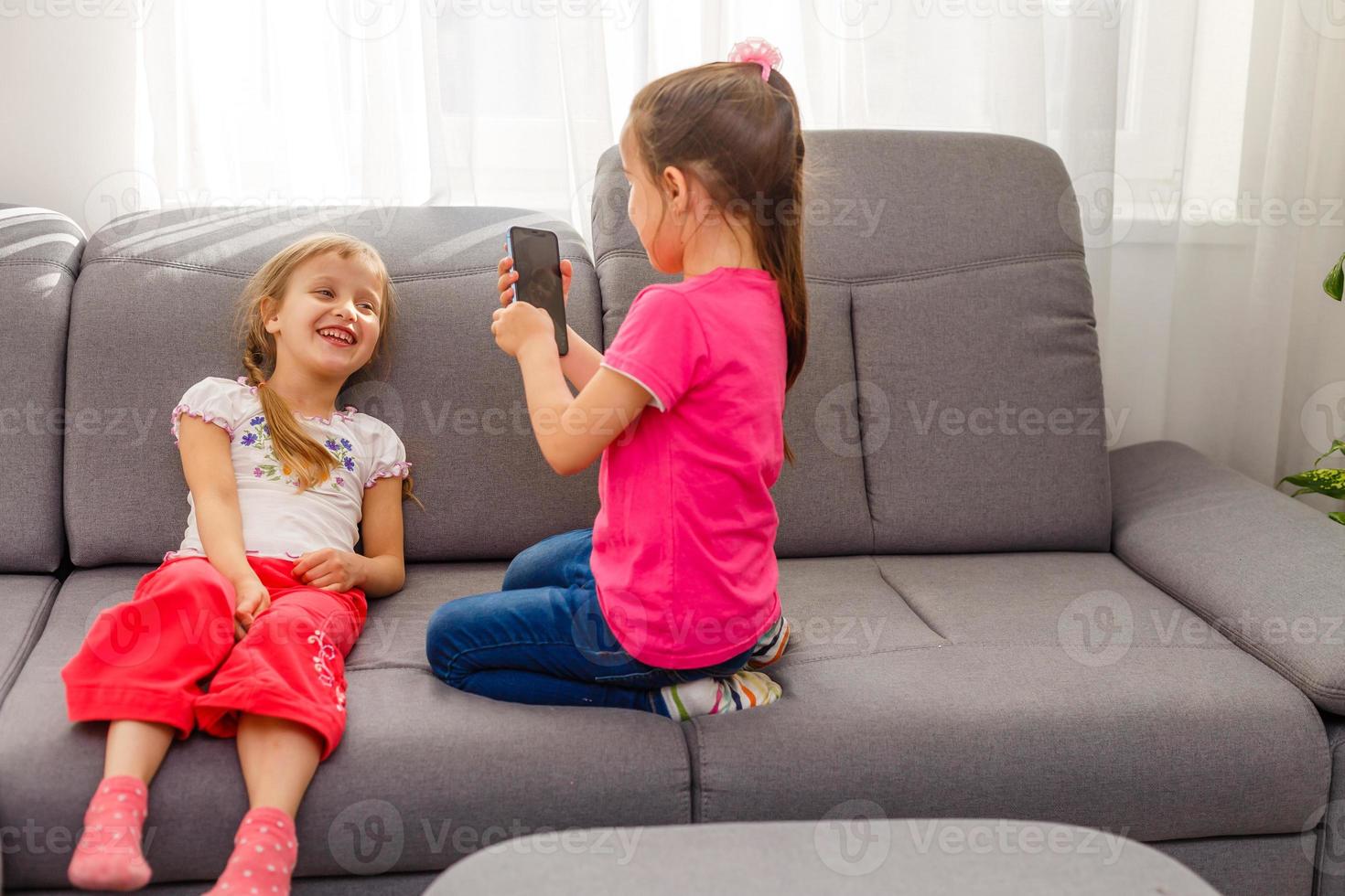 Stay Home Stay Safe. Two happy kids sitting on cozy chair relaxing playing in white living room indoors. Sisters having fun at home photo