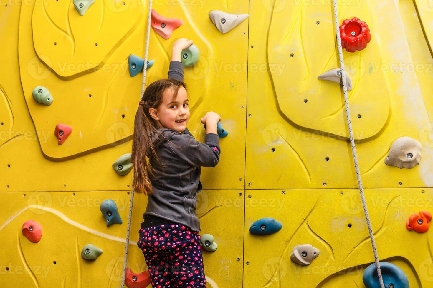 Little girl climbing a rock wall indoor photo