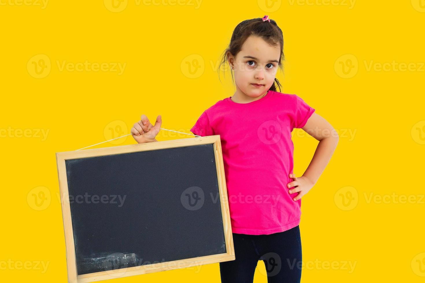 Cute little girl holding a chalkboard, isolated yellow background photo