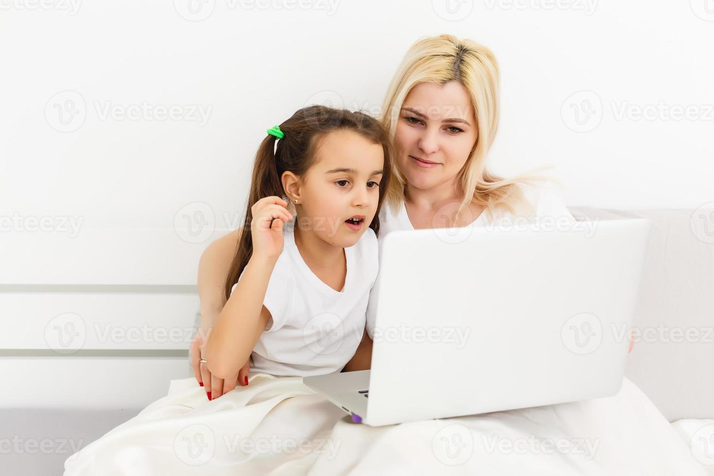 Young mother with toddler child working on the computer from home in bed photo