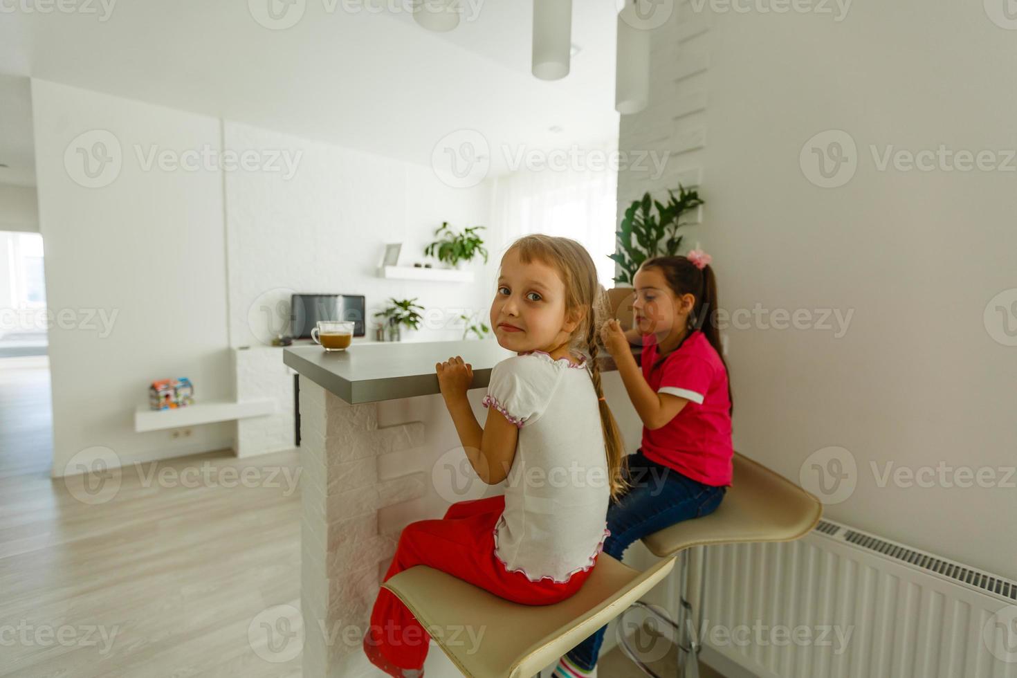 Stay Home Stay Safe. Two happy kids sitting on cozy chair relaxing playing in white living room indoors. Sisters having fun at home photo