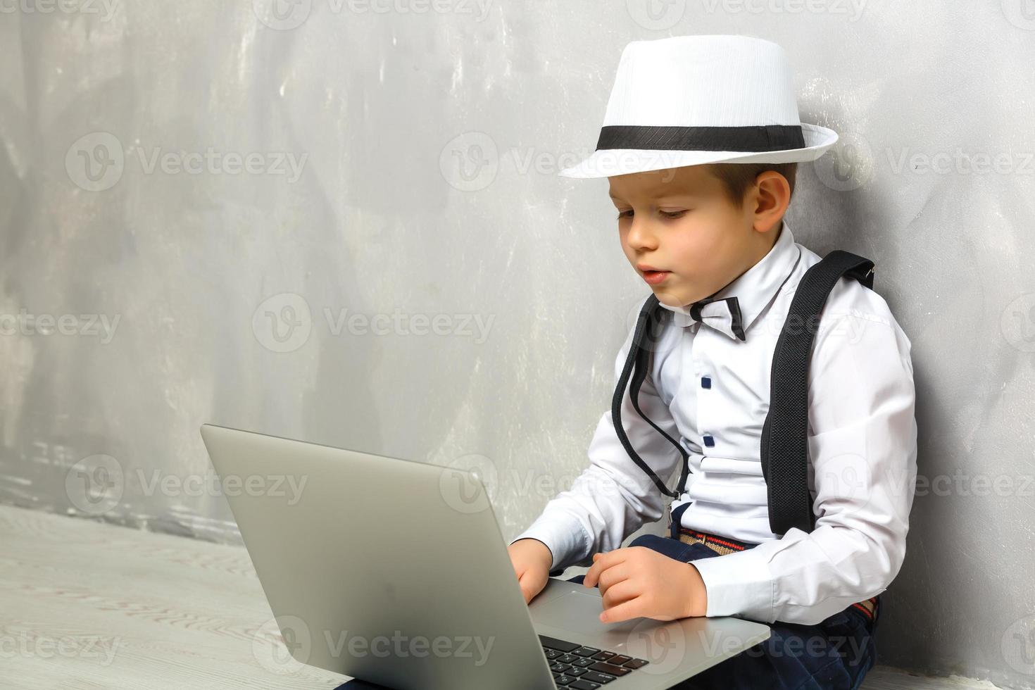 Portrait of Genius. Young boy working on the computer sitting On the floor. Studying. Online learning remotely. Distant school. Distance education. Online courses and knowledge. photo