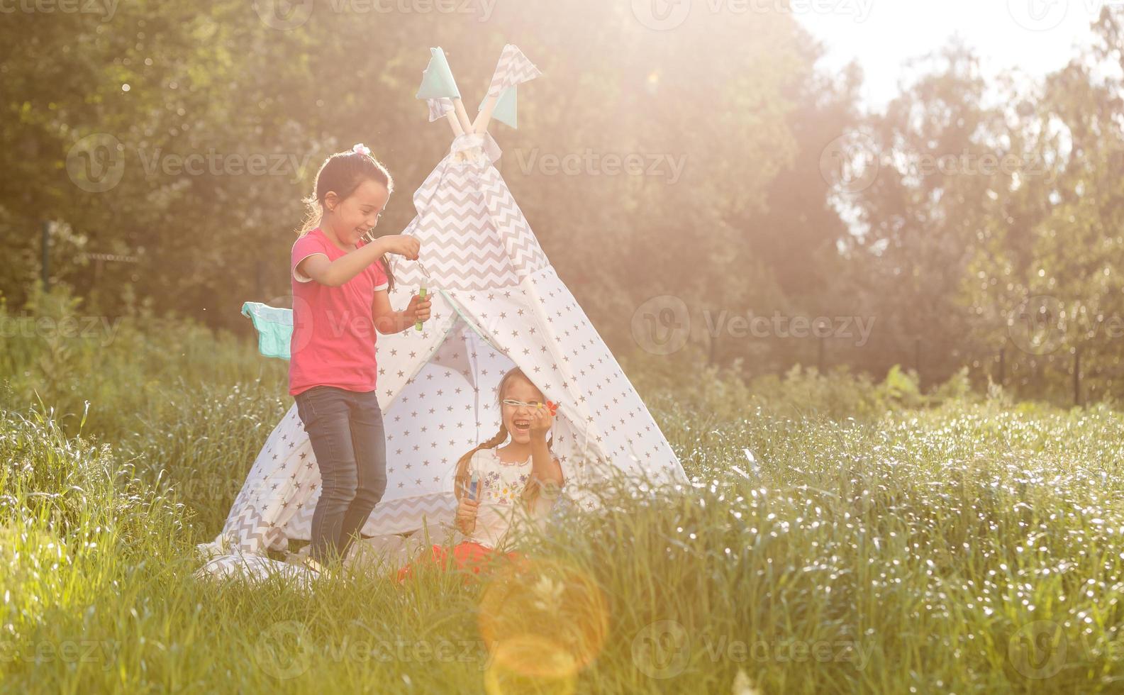Two happy laughing little girls in camping tent in dandelion field photo
