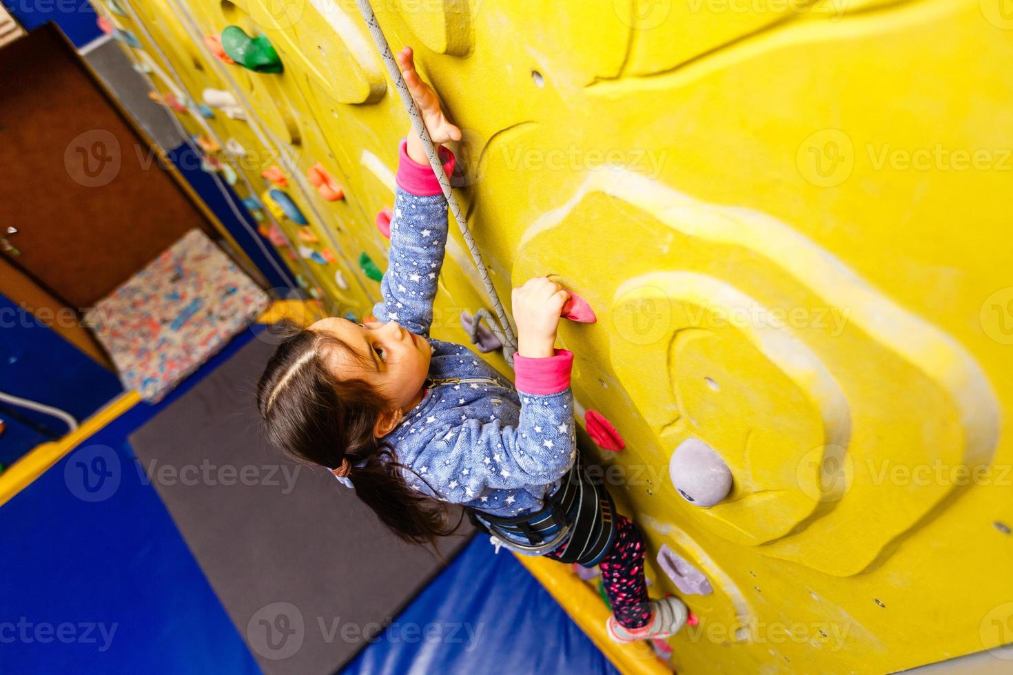 Little girl climbing a rock wall indoor photo