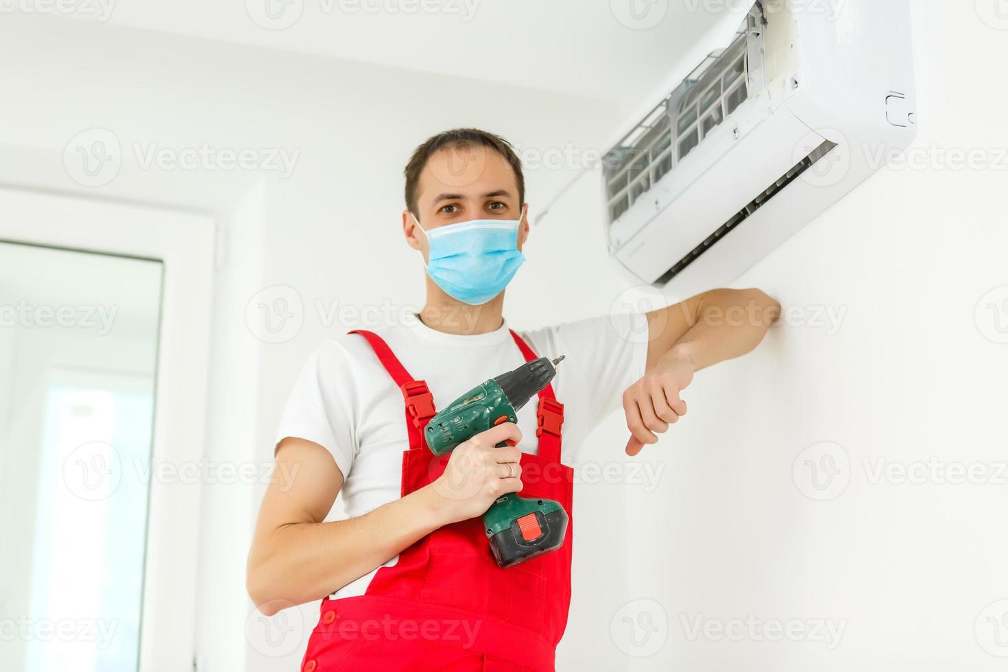 joven trabajador instala aire acondicionado en la habitación con paredes azules foto