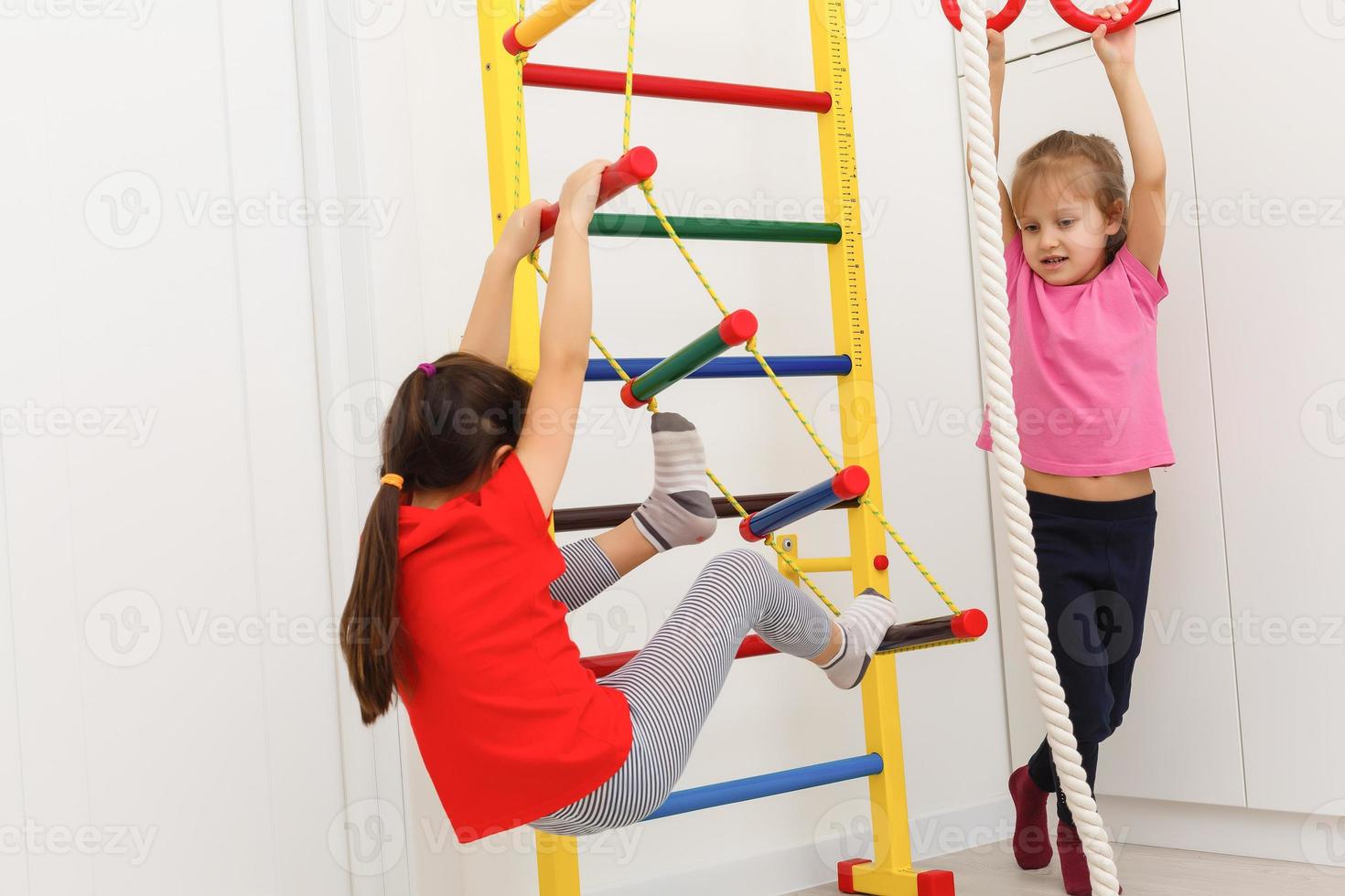 conceptos de actividad infantil. niñas caucásicas haciendo ejercicios de estiramiento en barras de pared en el interior.composición de imagen horizontal foto