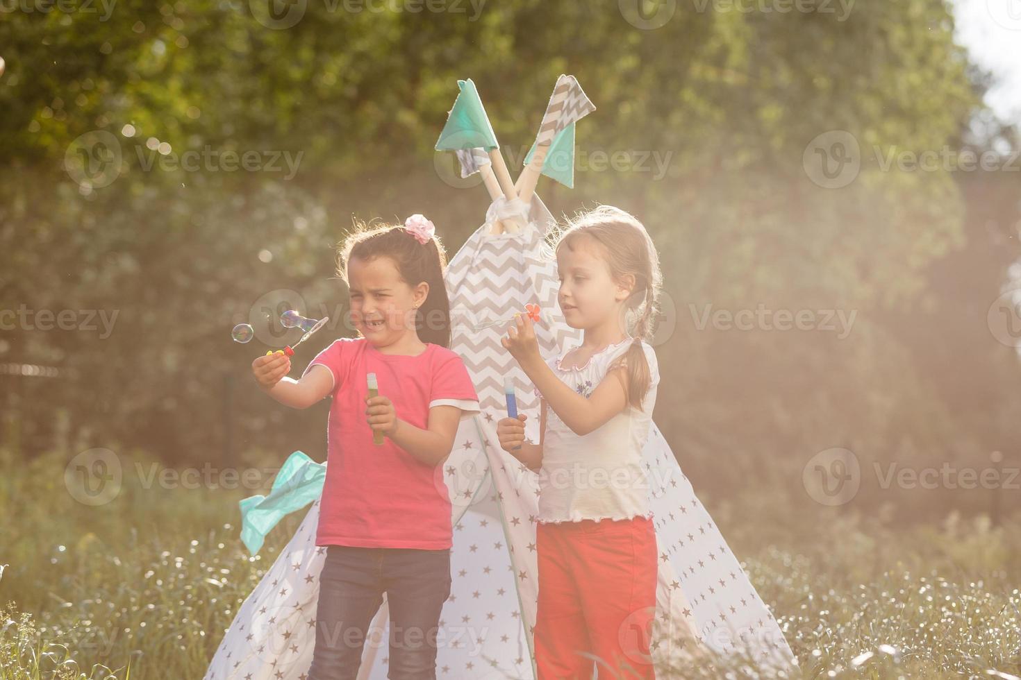 childhood and hygge concept - happy little girls playing in kids tent photo