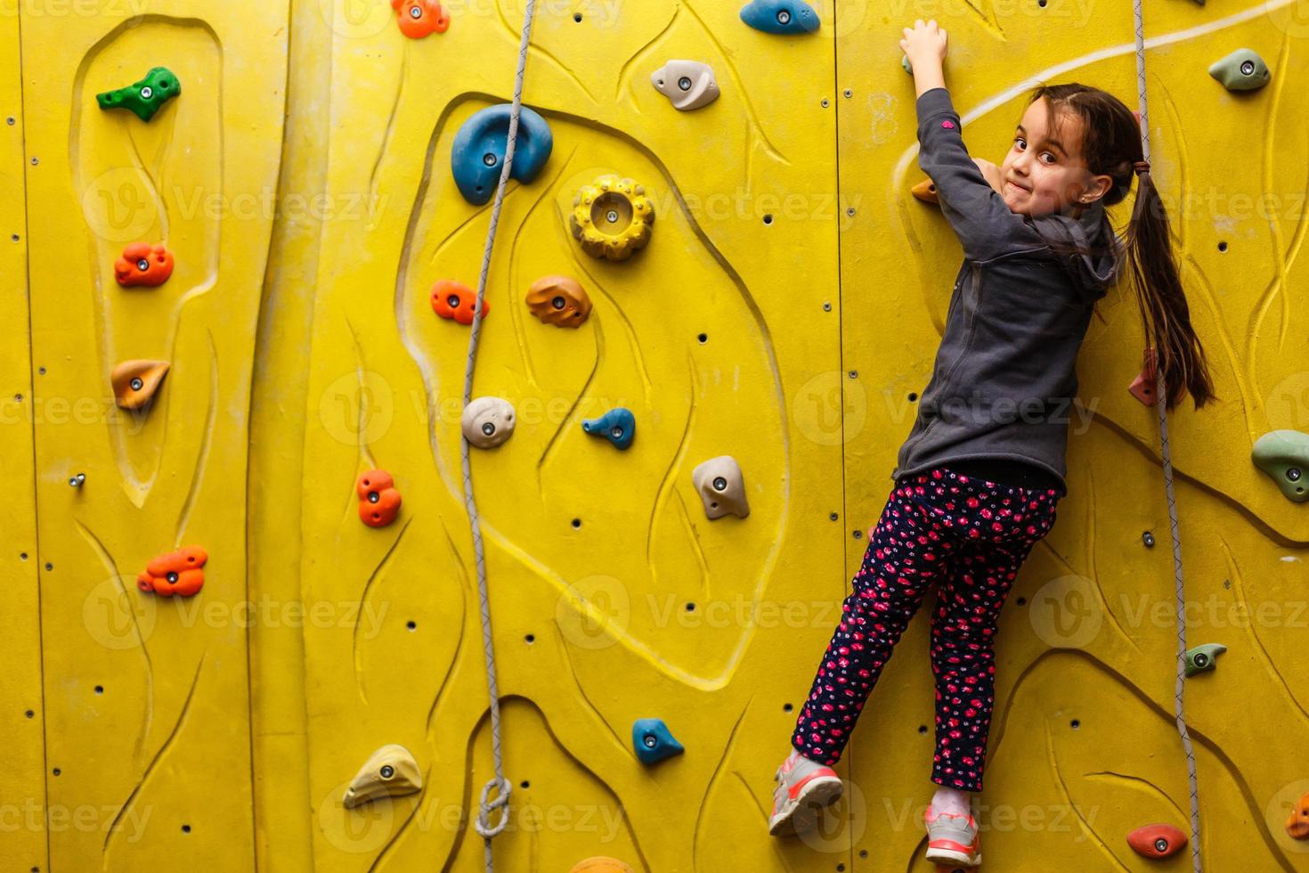 little girl climbing a rock wall indoor. photo
