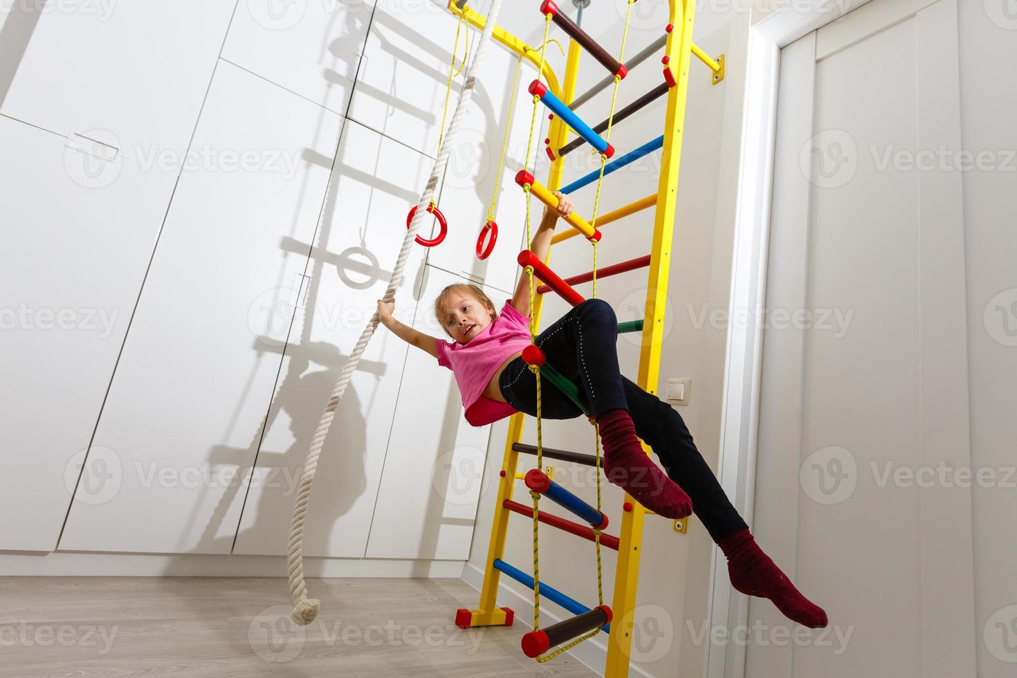 Little girl lifting legs on the wall bars photo