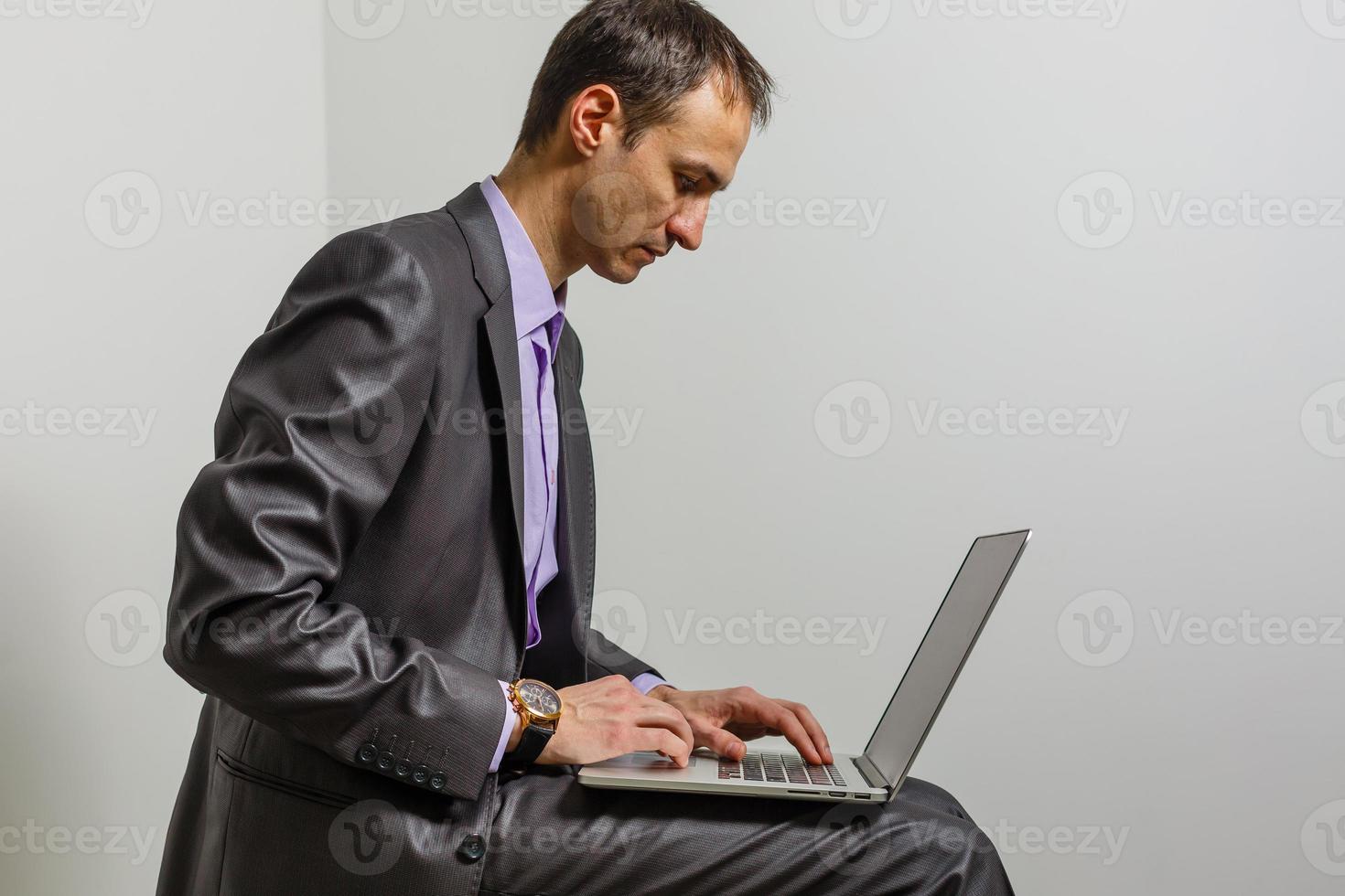 Positive young man using laptop computer over grey studio background photo
