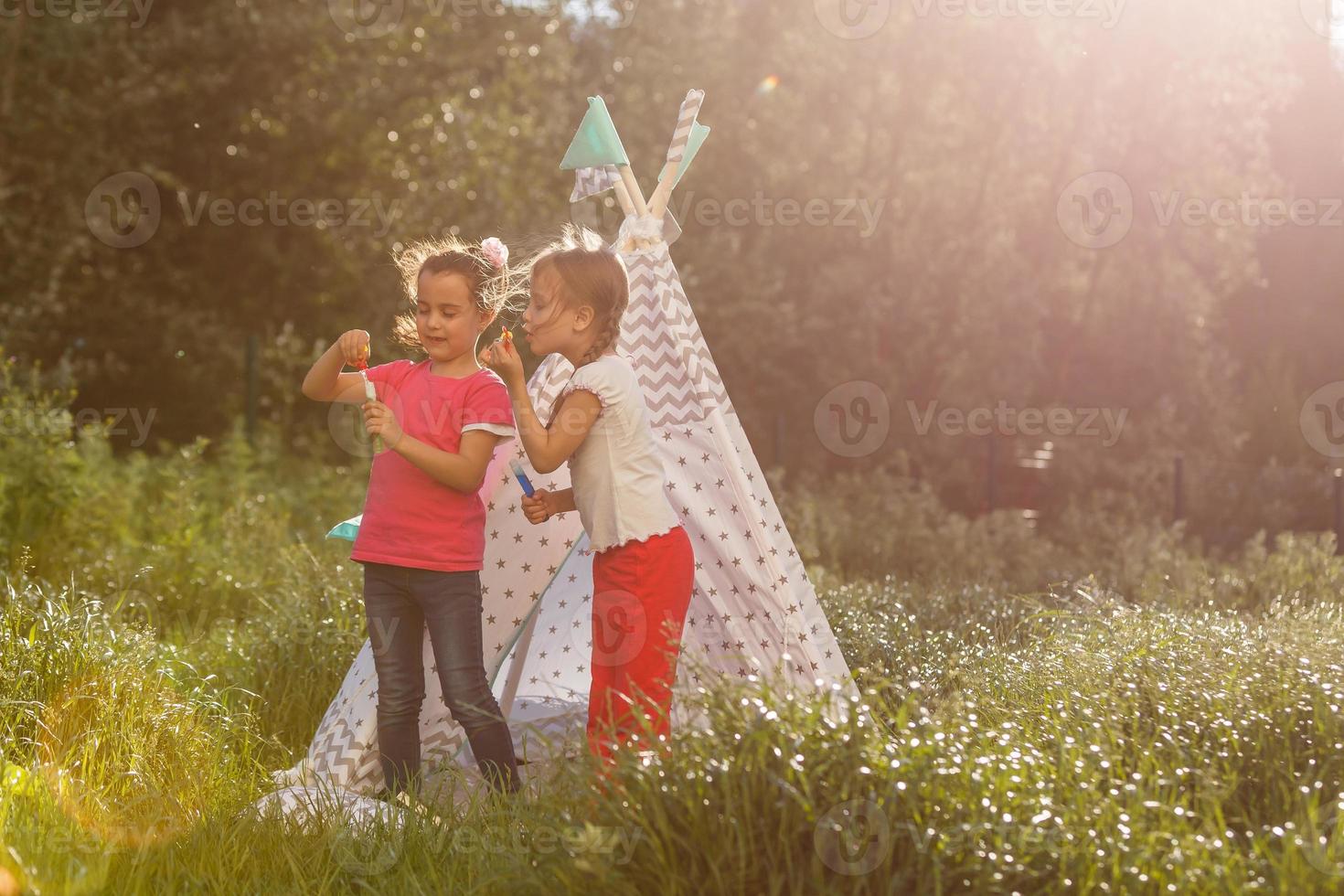 Two happy laughing little girls in camping tent in dandelion field photo