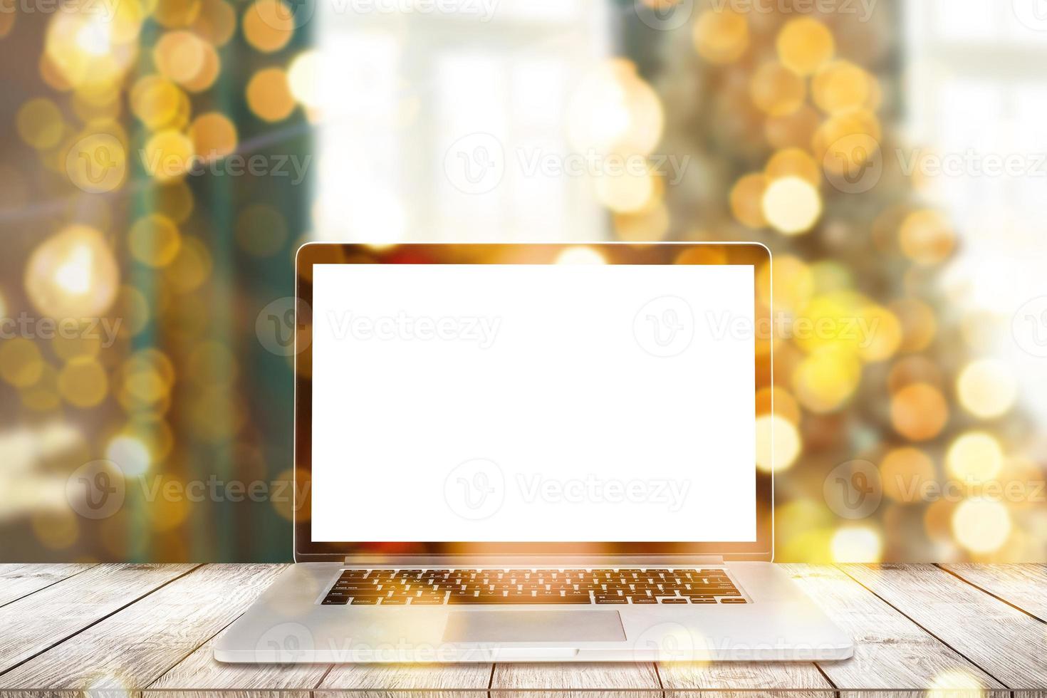 Image of open laptop with white screen on wooden table in front of christmas tree background. For mockup photo