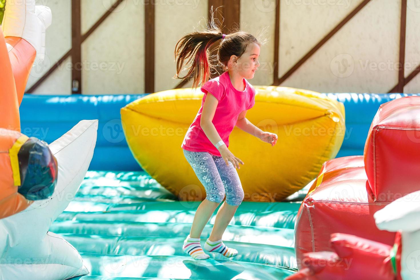 Child jumping on colorful playground trampoline. Kids jump in inflatable bounce castle on kindergarten birthday party Activity and play center for young child. Little girl playing outdoors in summer photo