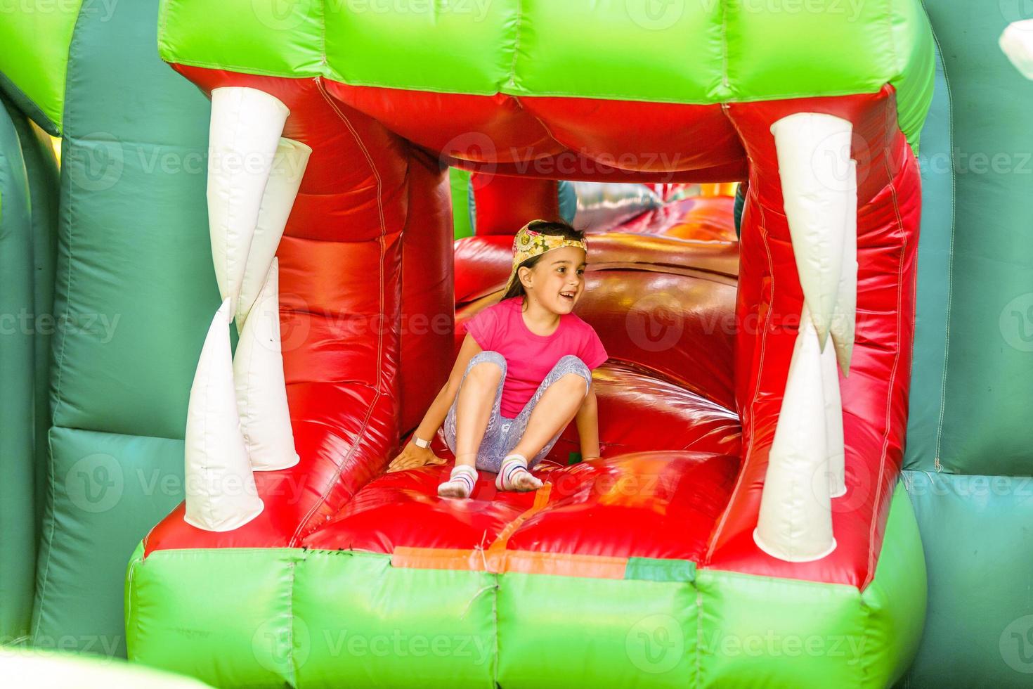 Cute funny preschool little girl in a colorful, jumping and bouncing in an inflatable castle having fun at a children birthday party on a kids playground in summer photo