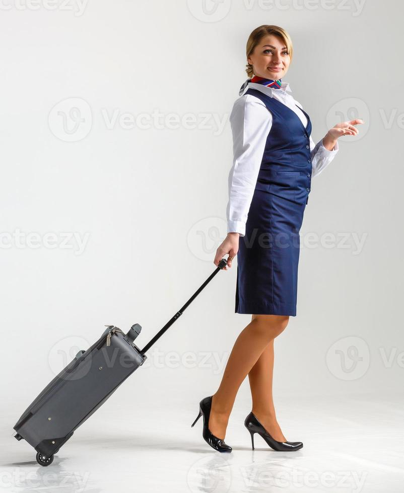 The stewardess goes and rolls her suitcase. White background photo